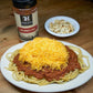 Bowl of seven hills chili over spaghetti noodles topped with shredded cheddar cheese