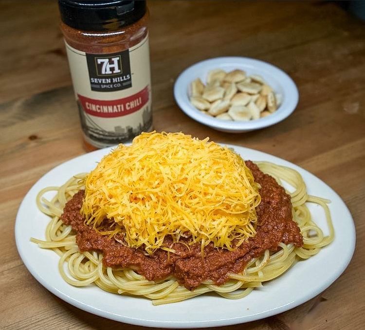Bowl of seven hills chili over spaghetti noodles topped with shredded cheddar cheese